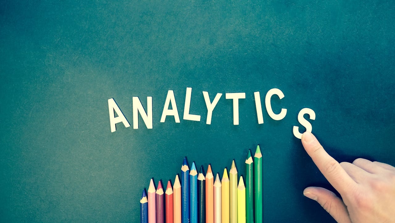 service-03 Colored pencils and letters spelling 'ANALYTICS' on a textured background with a hand.