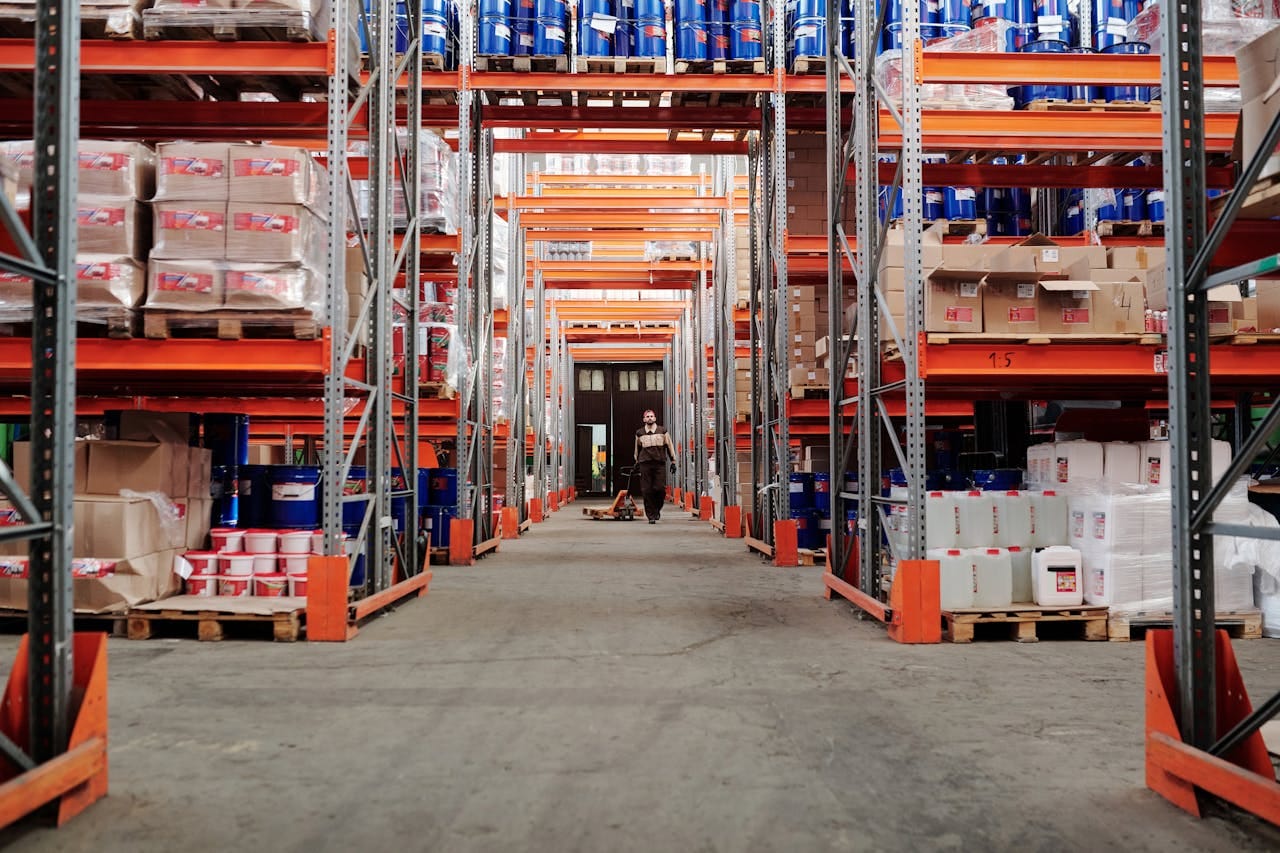 service-06 A spacious industrial warehouse with stocked shelves and a worker in protective gear.